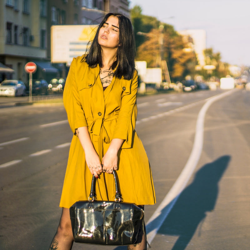 Woman in a yellow coat holding a black handbag on a city street.